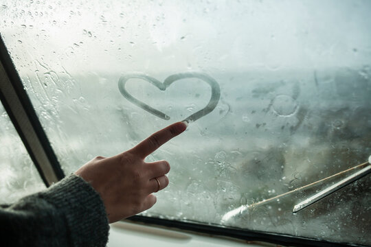 Woman's finger drawing a heart on the window of a van
