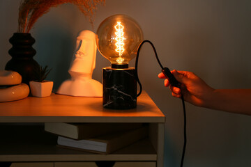 Woman turning on lamp on table