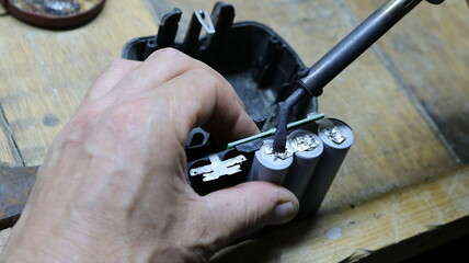 close-up of male hands with a small soldering iron welding contacts on old batteries from a...