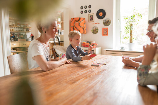 Family playing cards while sitting at dining table during weekend