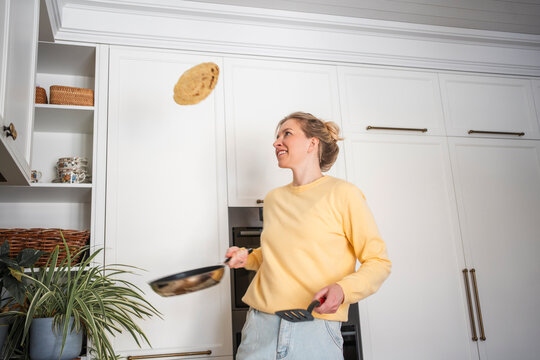 Woman flipping a pancake in a modern kitchen with plants and white cabinets