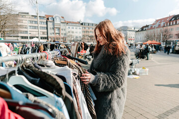 Red-haired woman at flea-market seaching for clothes