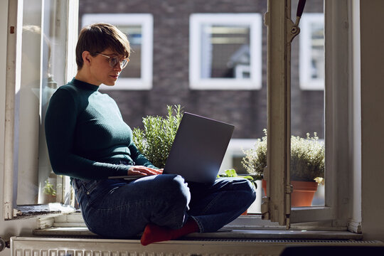Woman sitting at the window at home using laptop