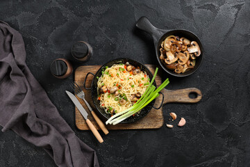 Frying pans with tasty pasta, mushrooms and spices on wooden background