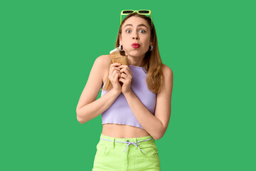 Surprised young woman with bitten vanilla ice cream in waffle cup on green background