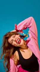 Woman in pink shirt biting cocktail glass with intense emotion on blue background. Concept of...