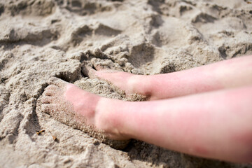 Sunlight casts gentle shadows on feet buried in soft, warm beach sand. Relaxation captures essence of peaceful coastal setting. Close-up highlights textures and natural tones