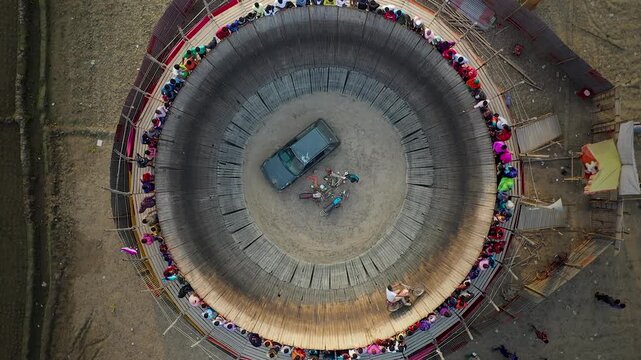 Bogura, Bangladesh - 16 August 2025: Aerial view of the Well of Death performance with a car and motorbikes, surrounded by spectators in a circular wooden structure.
