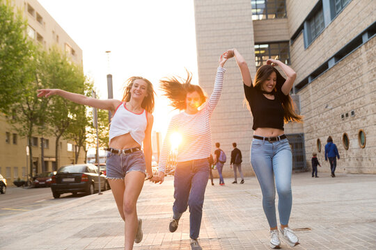 Three happy young women running hand in hand on sidewalk