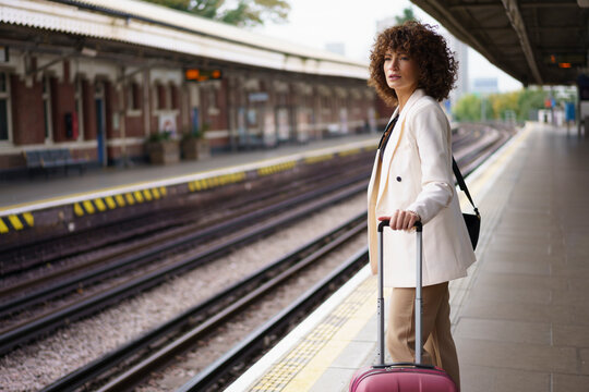 Businesswoman standing with suitcase and waiting at railroad station platform