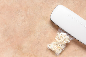 Vacuum sealer machine for food with chopped mushrooms in pack on beige grunge background