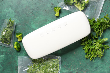Vacuum sealer machine for food with parsley and broccoli in packs on green grunge background