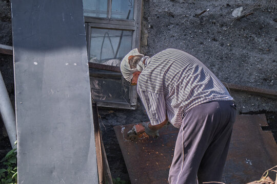 An older man using a grinder to work on a metal sheet outdoors.
