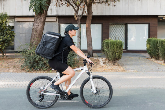 Female delivery person carrying backpack while riding cycle on road
