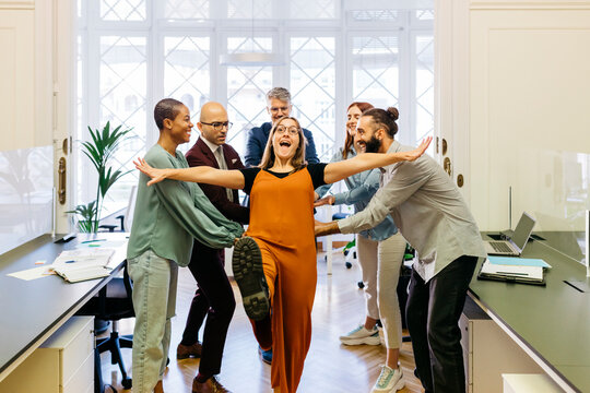 Cheerful businesswoman falling while coworkers catching at workplace