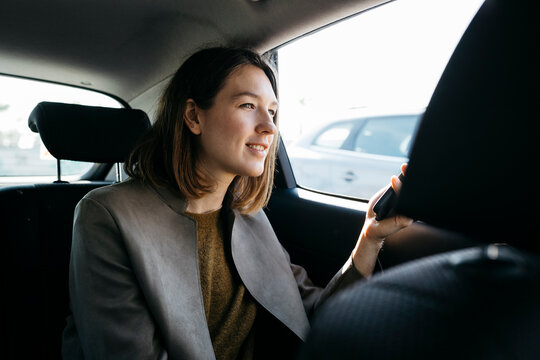 Smiling woman sitting in back seat of a car holding cell phone