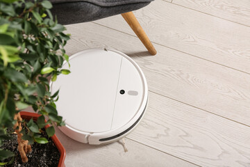 Modern robot vacuum cleaner on floor near armchair at home