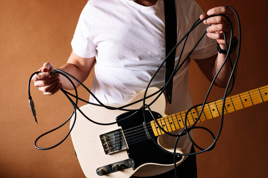 Mature male musician holding guitar against brown wall