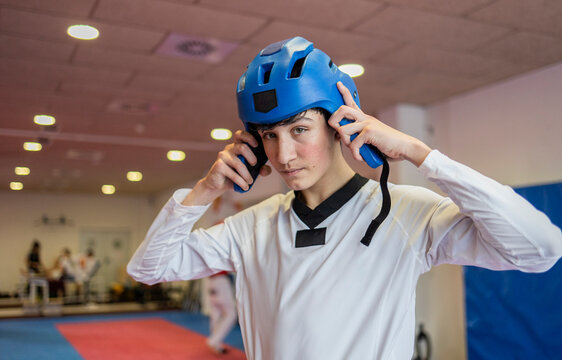Young man preparing for martial arts training indoors wearing a blue helmet