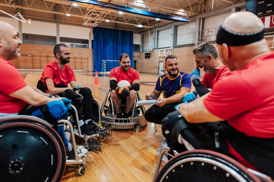Smiling trainer planning with disabled athletes sitting on wheelchair at sports court