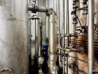 A wide-angle shot of a dense industrial piping system with a large vertical tank. The scene is a...
