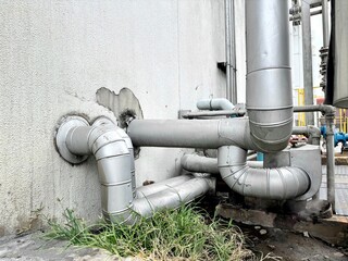  a complex industrial piping system exiting a concrete wall. The large, insulated pipes with...
