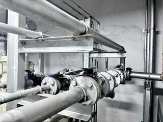 series of industrial pipes, valves, and metal supports running along a wall. The pipes and fittings...