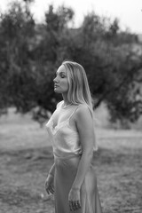 Blonde woman swinging her hair joyfully in natural field at golden sunset near olive trees, highlighting natural beauty, healthy hair, serenity, and connection with nature outdoors.