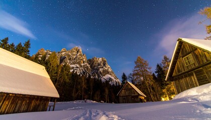 A Stunning Night Sky Over Snowy Mountain Cabins, Featuring A Beautiful Starry Night Scene With Illuminated Wooden Structures, Ideal For Winter And Travel Photography.