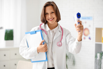 Beautiful female doctor with infrared thermometer and clipboard in clinic