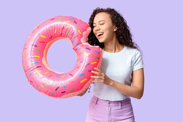 Beautiful young African-American woman with inflatable ring on lilac background