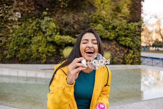 Happy young woman enjoying blowing bubbles at footpath