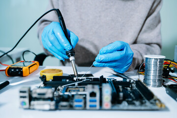 Closeup of technician soldering a computer motherboard with precision tools, showcasing electronics...