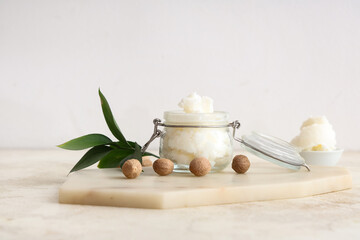 Glass jar with shea butter and nuts on table against light background