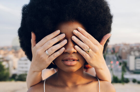 Woman covering eyes of Afro girlfriend with hands at sunset
