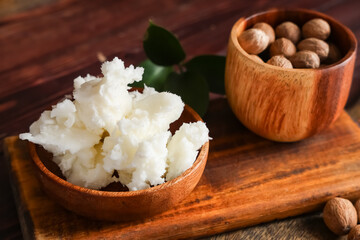Board with bowls of shea butter and nuts on wooden table, closeup
