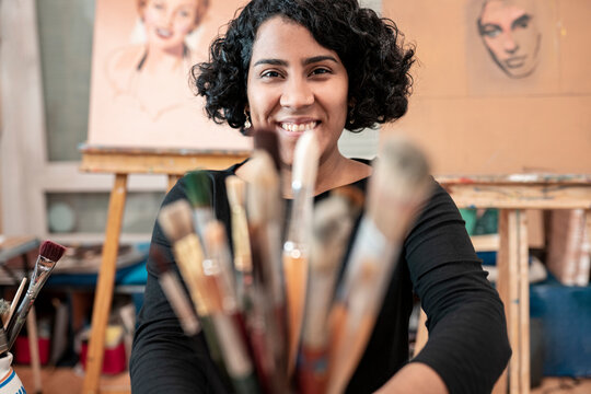 Smiling young female painter with paintbrushes at art studio