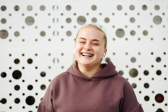 Smiling young woman wearing bluetooth in front of wall