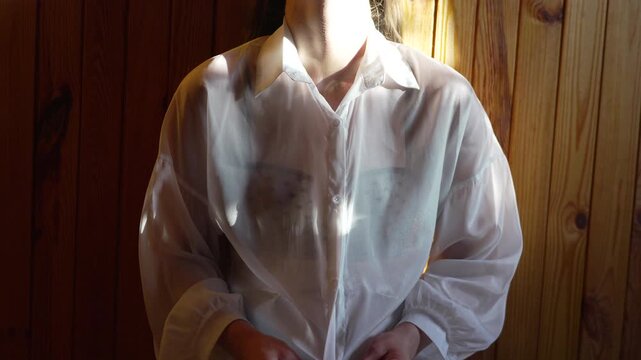Woman unbuttoning shirt in sunlight against a wooden wall. Morning casual dressing