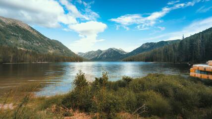 A peaceful lake nestled among tall mountains and lush forests, reflecting the serene blue sky and...
