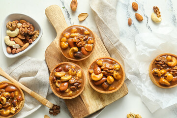 Tasty tarts with different nuts and caramel on wooden board against grunge white background