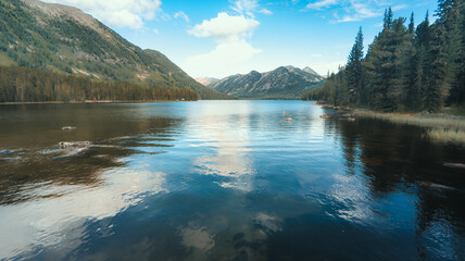 A serene landscape with a calm lake, green pine trees, and mountains reflected in the water creates a peaceful and tranquil setting, highlighting a connection with nature.