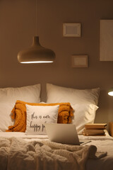 Laptop with stack of books on bed in dark bedroom at night