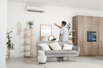 Handsome young man turning on air conditioner in living room, back view