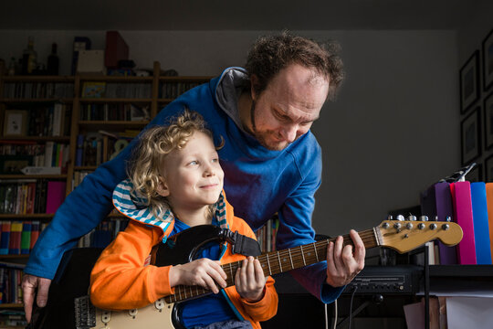 Man teaching guitar to smiling son looking away at home
