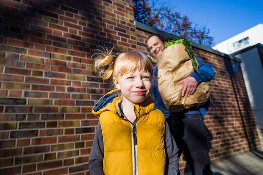 Cute blond girl standing against father carrying vegetables bag