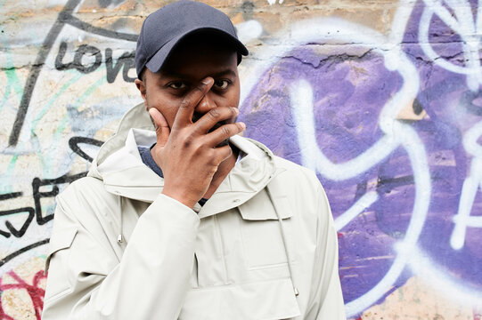 Portrait of man cin front of graffiti wall overing face with his hand
