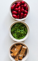 Three white plates with multi coloured herbs and berries, which are picked in a garden. 
