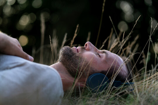 Relaxed man lying in field listening to music with headphones - Powered by Adobe