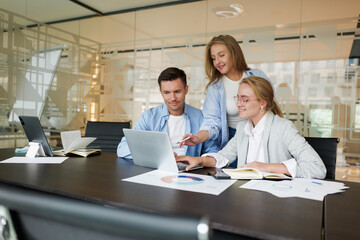 Collaborative professionals brainstorming in a modern office setting with charts and laptops